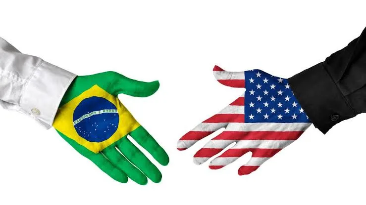 Duas mãos estendidas para um aperto de mão, pintadas com as bandeiras do Brasil e dos Estados Unidos, ilustrando o impacto do tarifaço americano nas exportações.