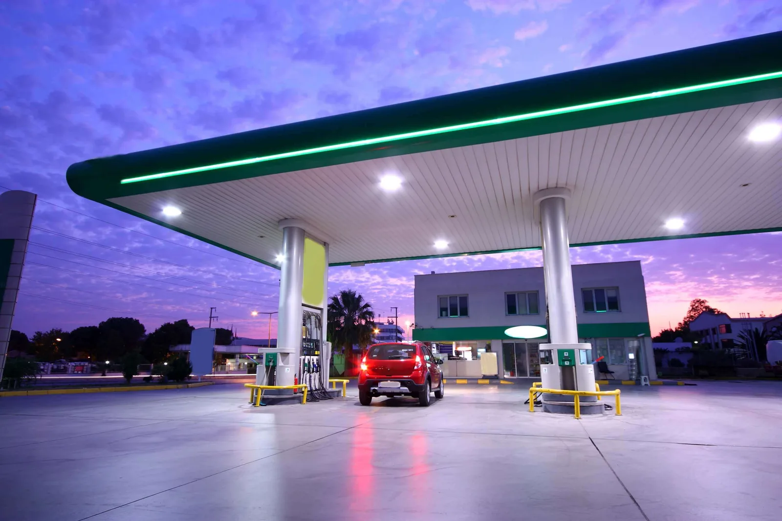 Carro vermelho abastecendo em um posto de combustível ao entardecer, cenário ideal para avaliar a margem de lucro na nota fiscal.