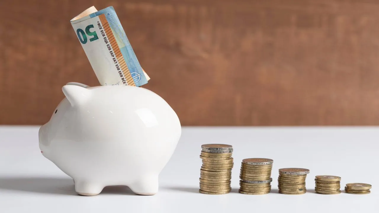 Cofrinho branco em formato de porquinho com notas e pilhas de moedas ao lado, ilustrando o controle financeiro que o Split Payment no Pix traz para o caixa da empresa.