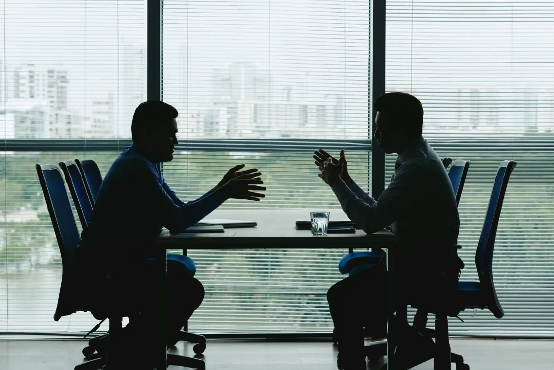 Silhuetas de dois executivos reunidos em uma sala de reunião corporativa para discutir a recuperação judicial e dívidas empresariais.