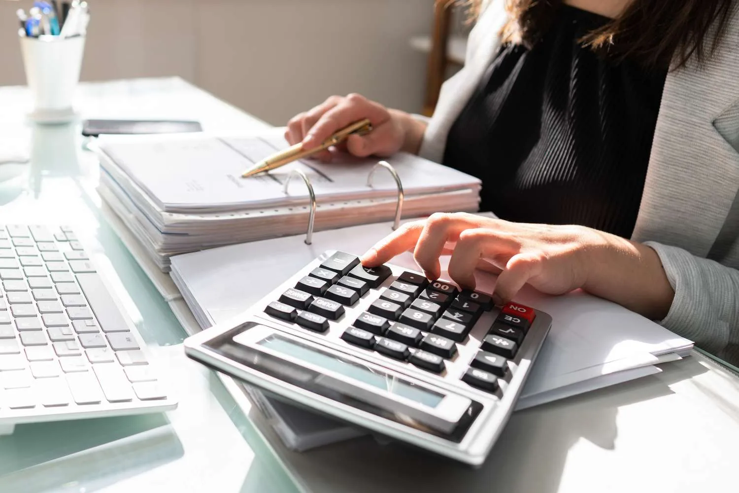 Contadora calcula impostos e revisa documentos financeiros em sua mesa de trabalho, destacando a importância do profissional diante da Reforma Tributária.