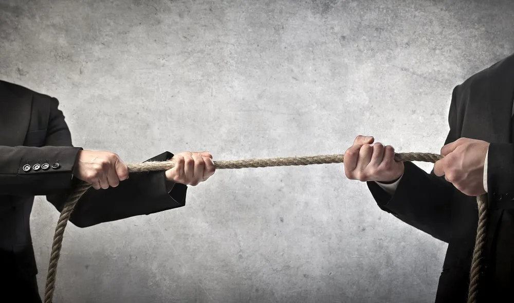 Duas pessoas de terno puxando uma corda em lados opostos, representando um litígio empresarial que pode ser resolvido por arbitragem tributária.