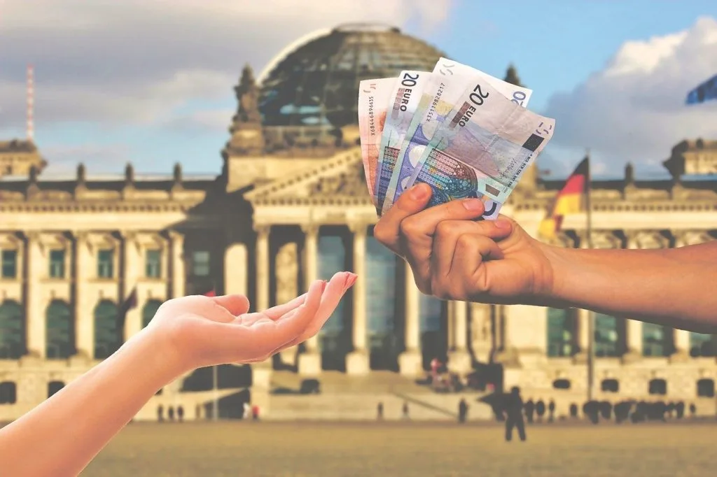 Mãos segurando notas de dinheiro em frente a um grande edifício público, ilustrando a recuperação de créditos tributários como a exclusão do ISS da base de PIS e COFINS.