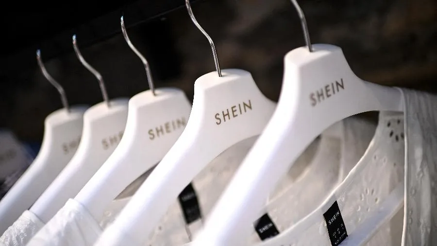 Cabides brancos com a marca Shein pendurados em uma arara, ilustrando compras de roupas afetadas pela taxa das blusinhas.
