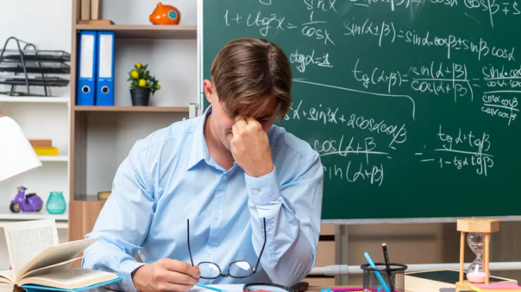 Homem de camisa azul sentado à escrivaninha com a mão no rosto, representando a incerteza e a complexidade das alíquotas da Reforma Tributária para 2027.