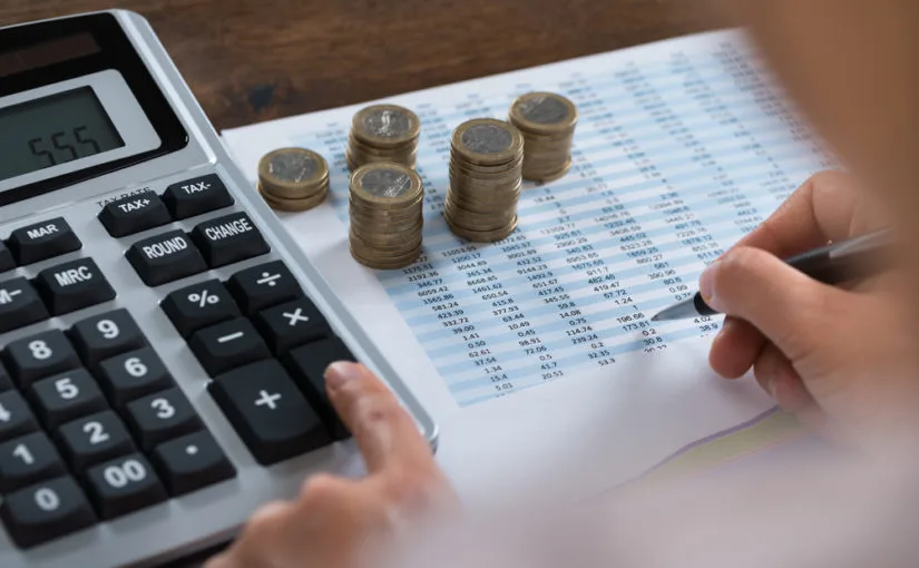 Calculadora, pilhas de moedas e planilhas sobre a mesa ilustram a preparação das empresas para a IFRS 20.