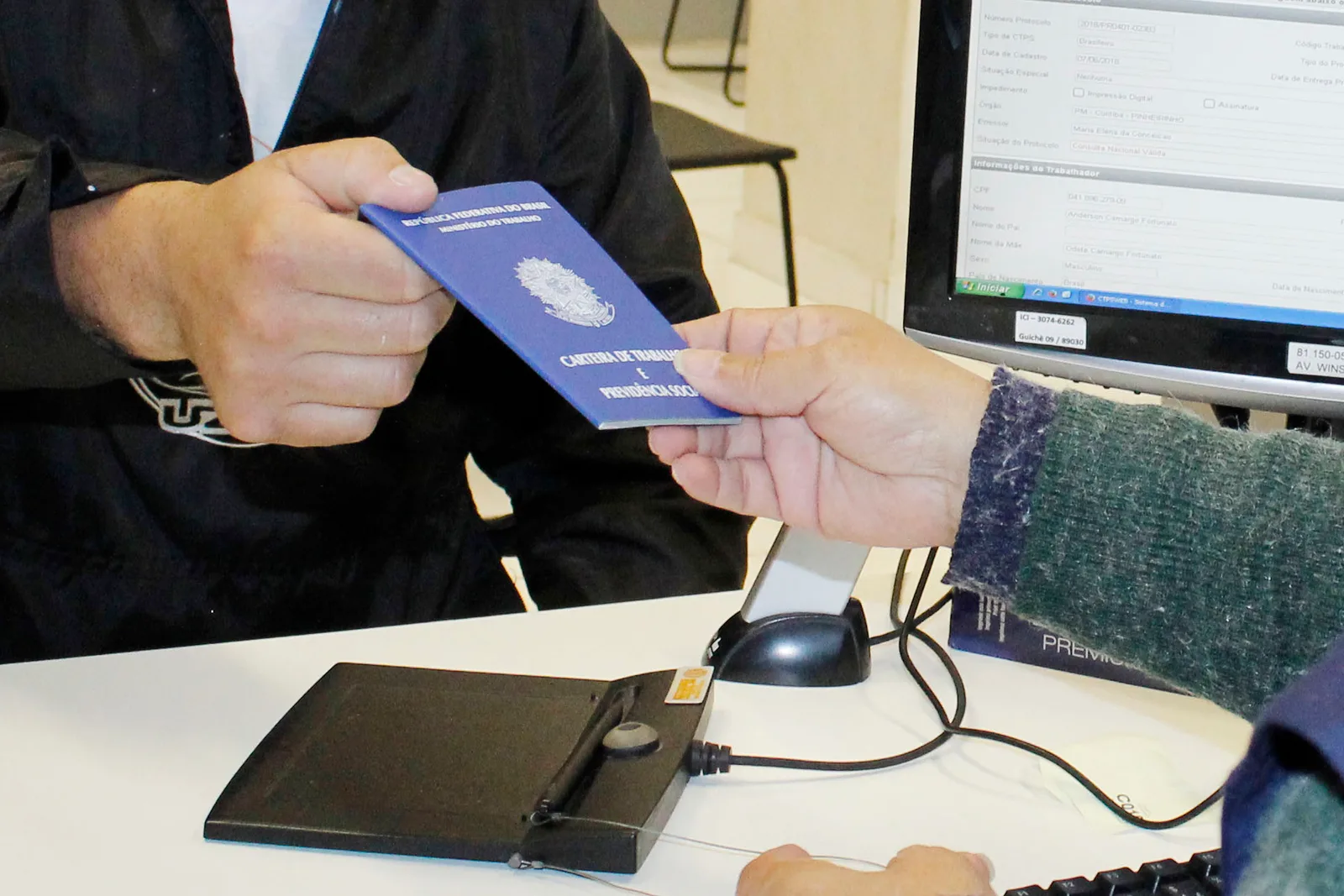 Pessoa entregando uma carteira de trabalho azul em um balcão de atendimento, representando a transição de trabalhadores CLT para MEI.