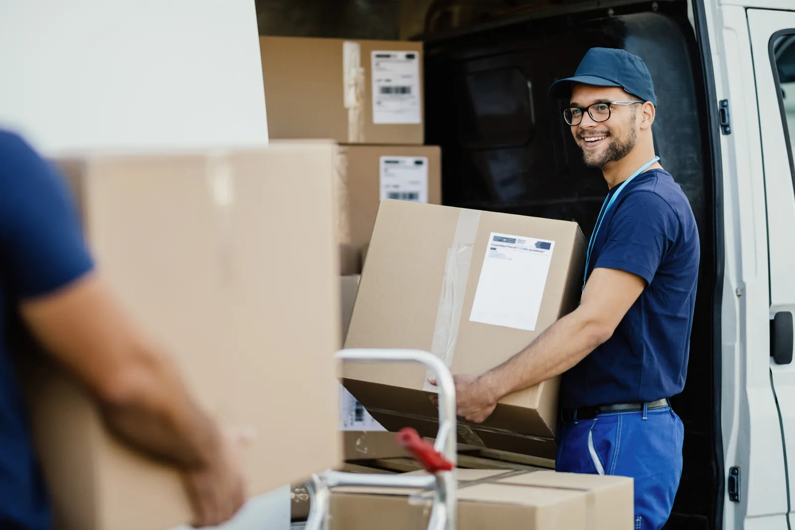 Entregador sorridente descarregando caixas de papelão de uma van, ilustrando o setor de distribuição que precisa revisar contratos com a Reforma Tributária.