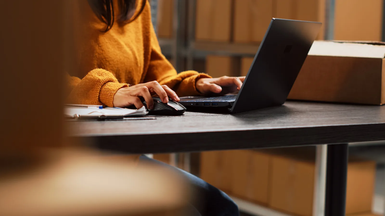Profissional trabalha com notebook e mouse em mesa de escritório, ilustrando a revisão de contratos na indústria e distribuição devido à Reforma Tributária.