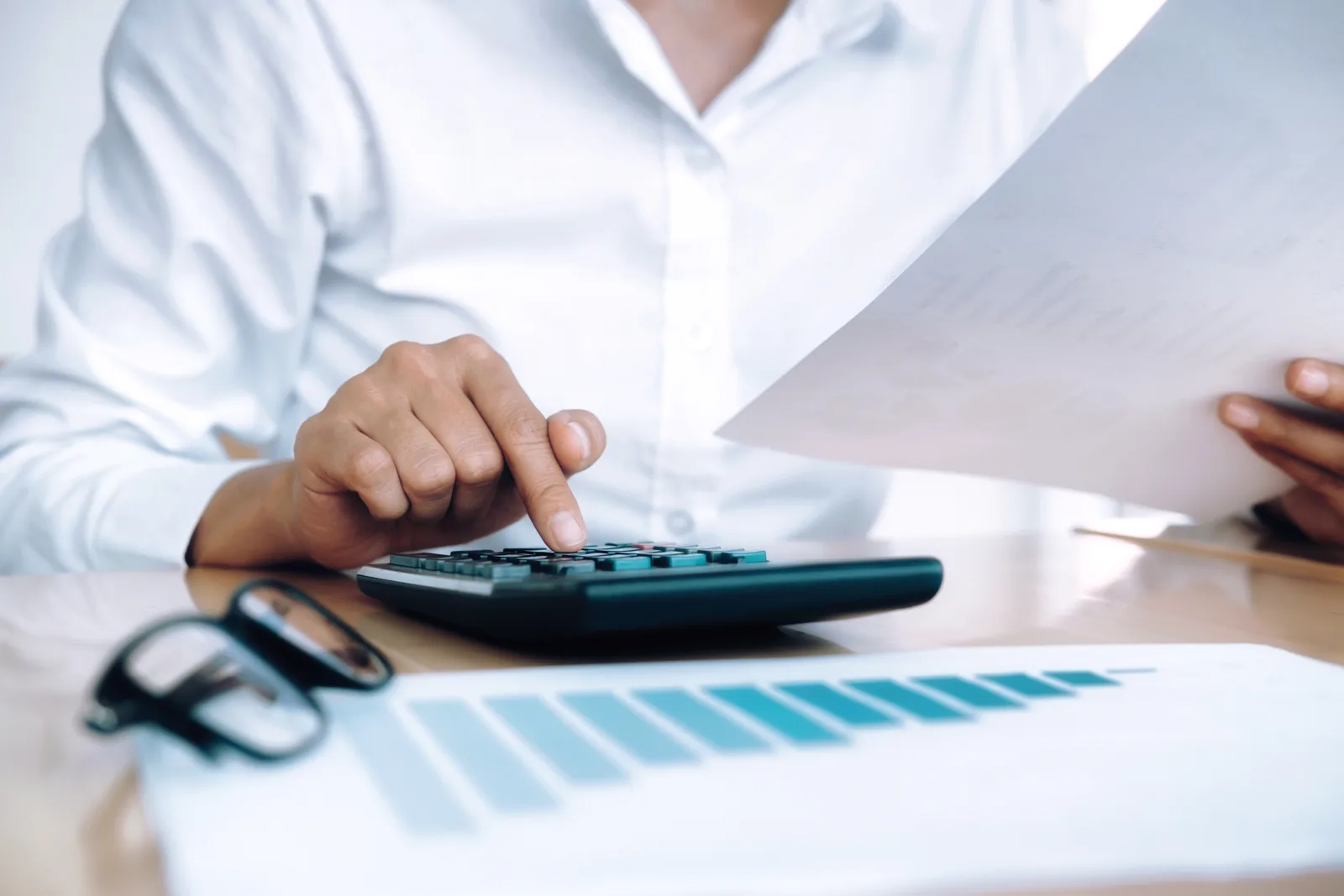 Pessoa de camisa branca usando calculadora e analisando documentos financeiros para calcular o pagamento de parcelas atrasadas do FGTS Digital.