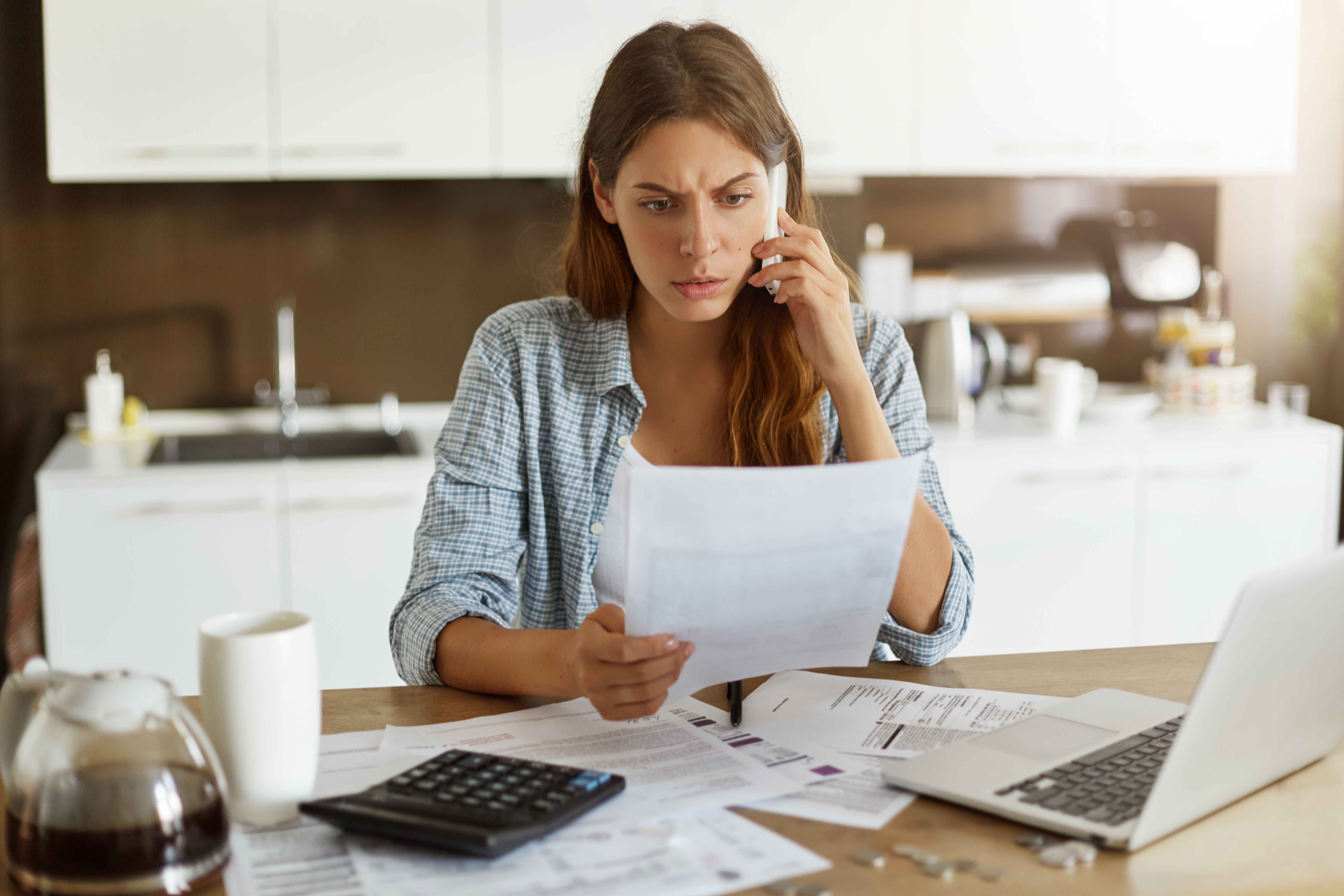 Mulher preocupada analisa contas e documentos financeiros ao telefone, ilustrando o impacto da alta carga tributária nos negócios.