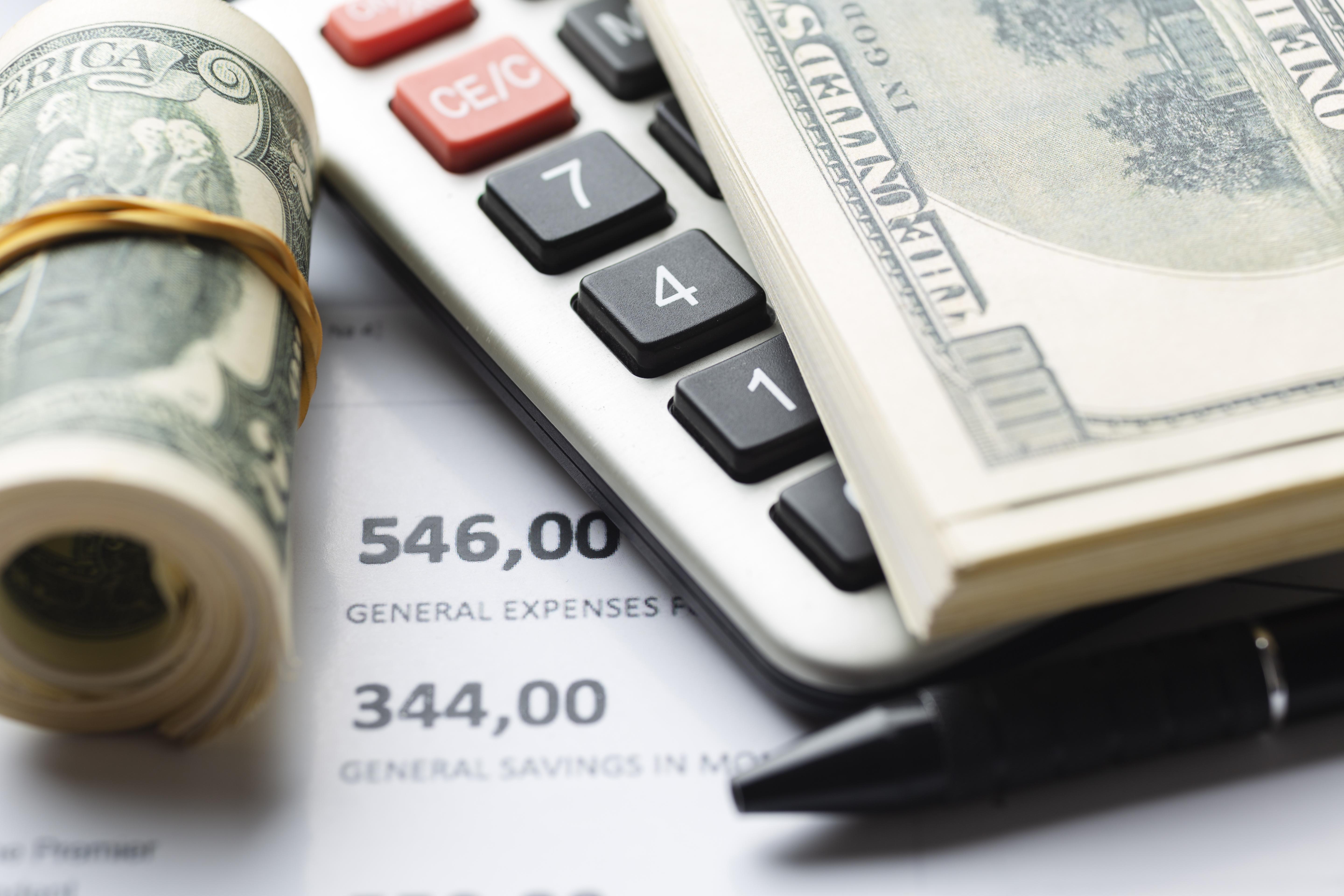 Calculadora, notas de dólar e uma caneta sobre documentos financeiros, ilustrando o impacto da alta carga tributária no Brasil sobre negócios globais.