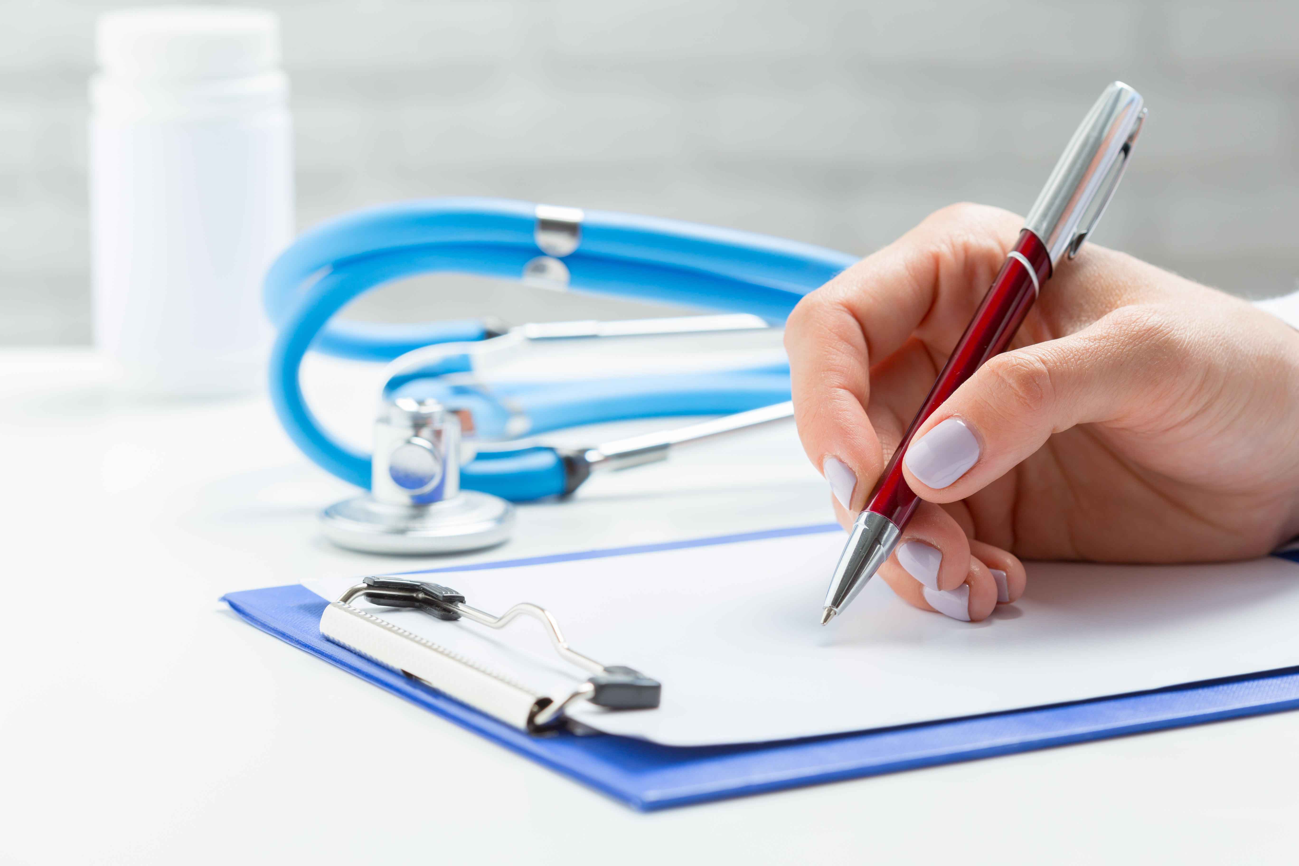 Mão escrevendo em prancheta com estetoscópio ao fundo, ilustrando a concessão de auxílio-doença pelo INSS sem necessidade de perícia médica presencial.