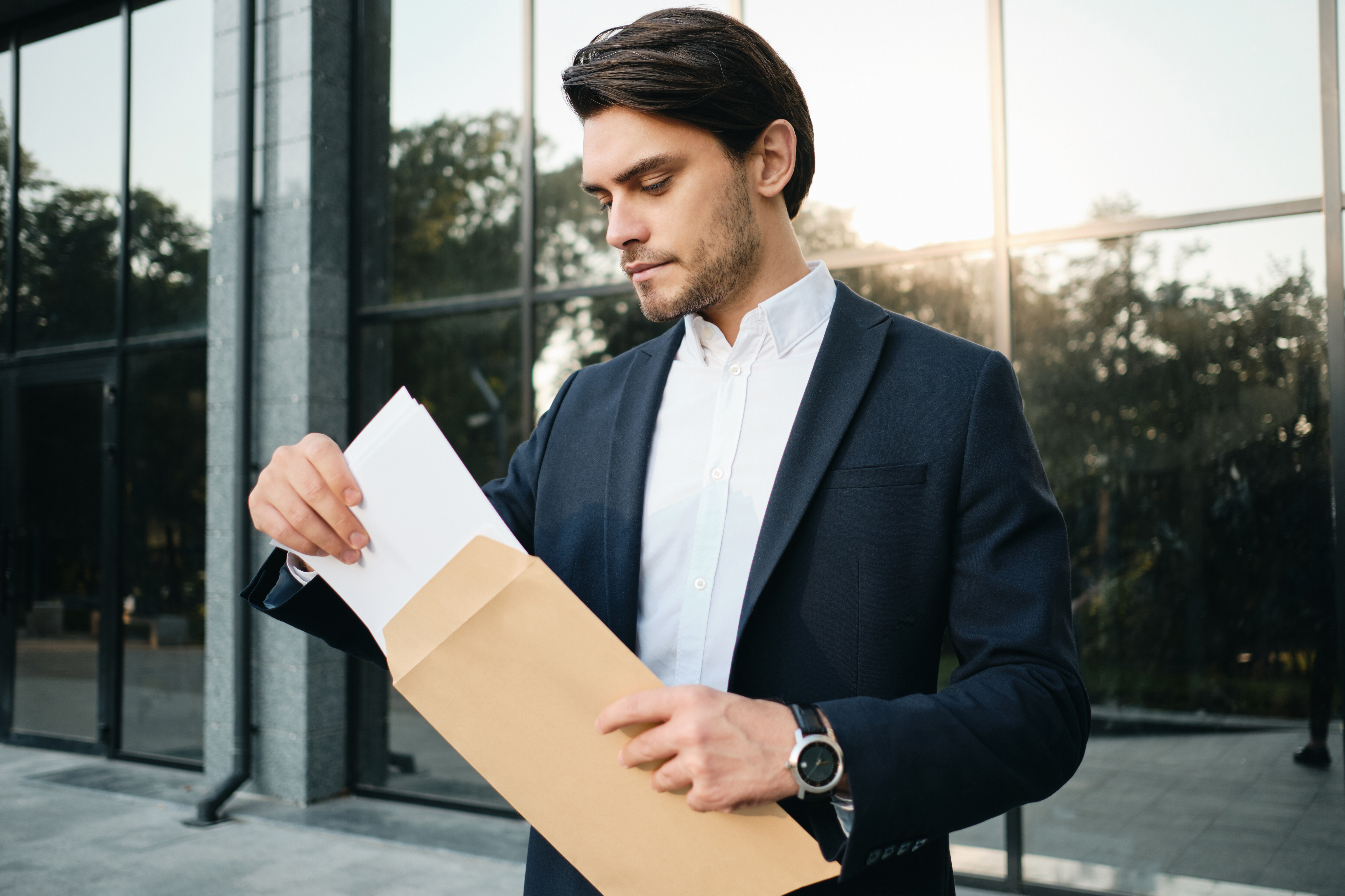 Homem de terno abre uma correspondência em frente a um prédio corporativo, lembrando que empresa sem movimento ainda tem obrigações fiscais.