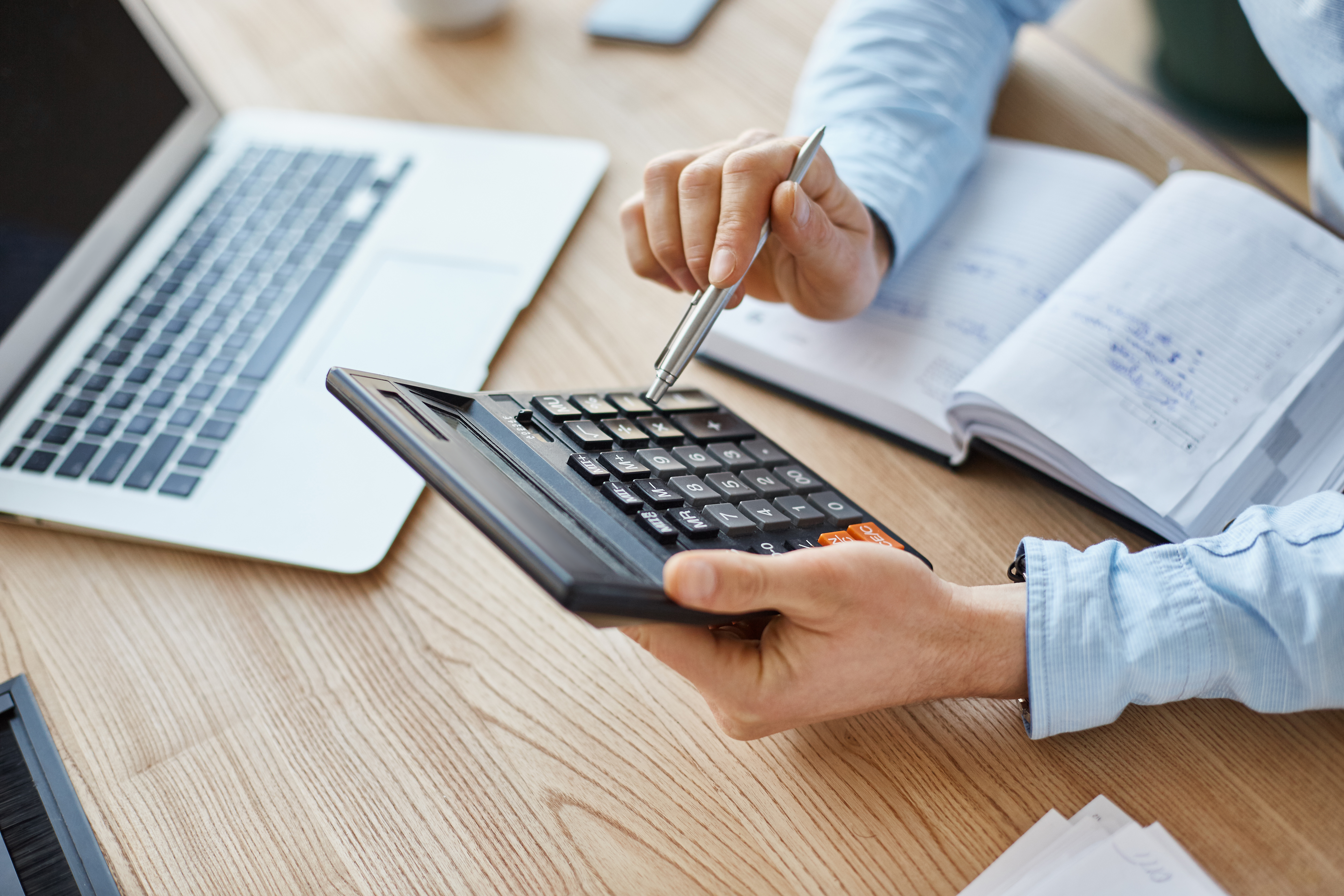 Empreendedor calculando custos e viabilidade financeira com calculadora, notebook e caderno em mesa de madeira para abrir franquia barata.