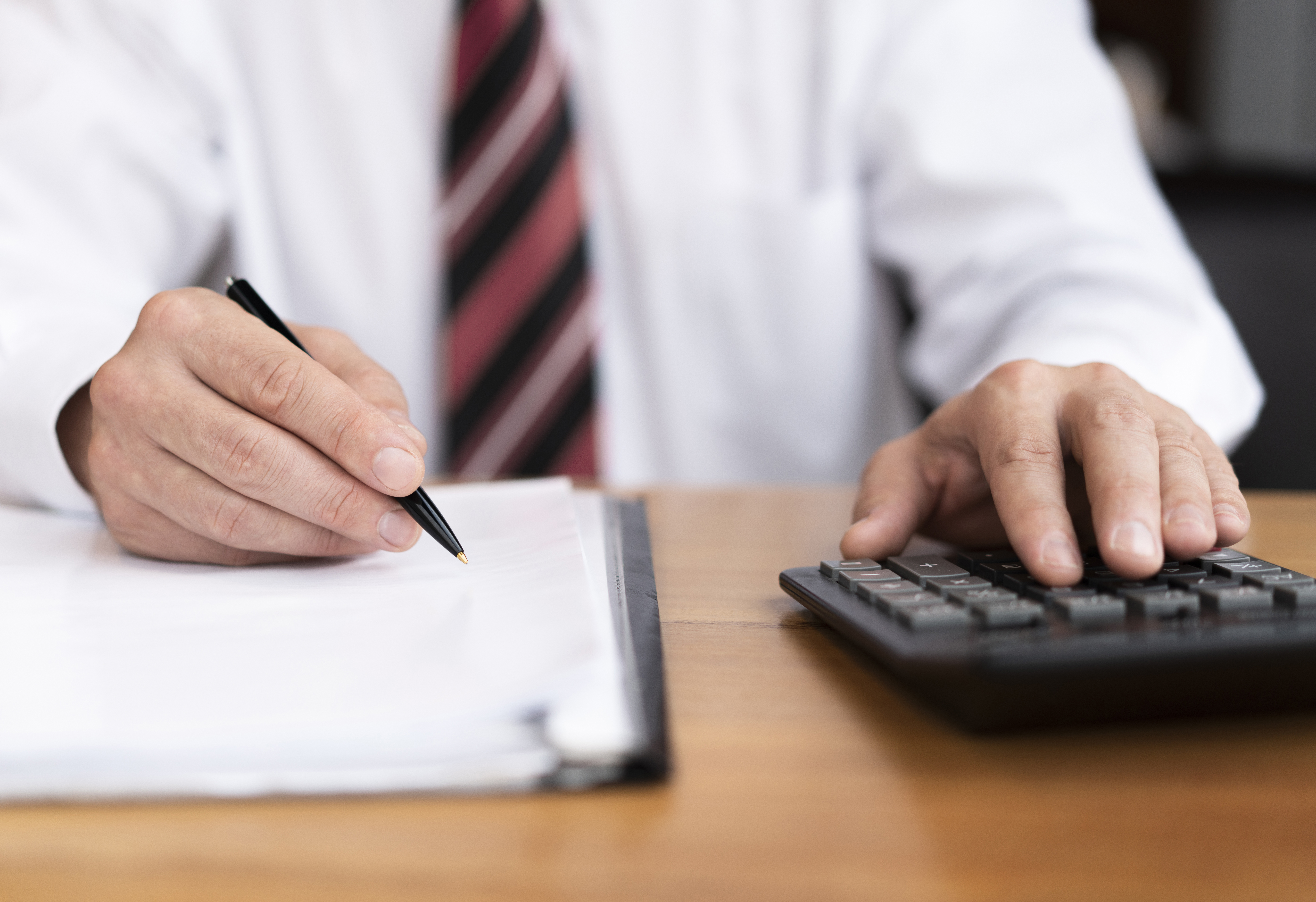 Profissional de terno usa calculadora e anota em documentos, ilustrando os riscos e exceções nos benefícios fiscais da reforma tributária.