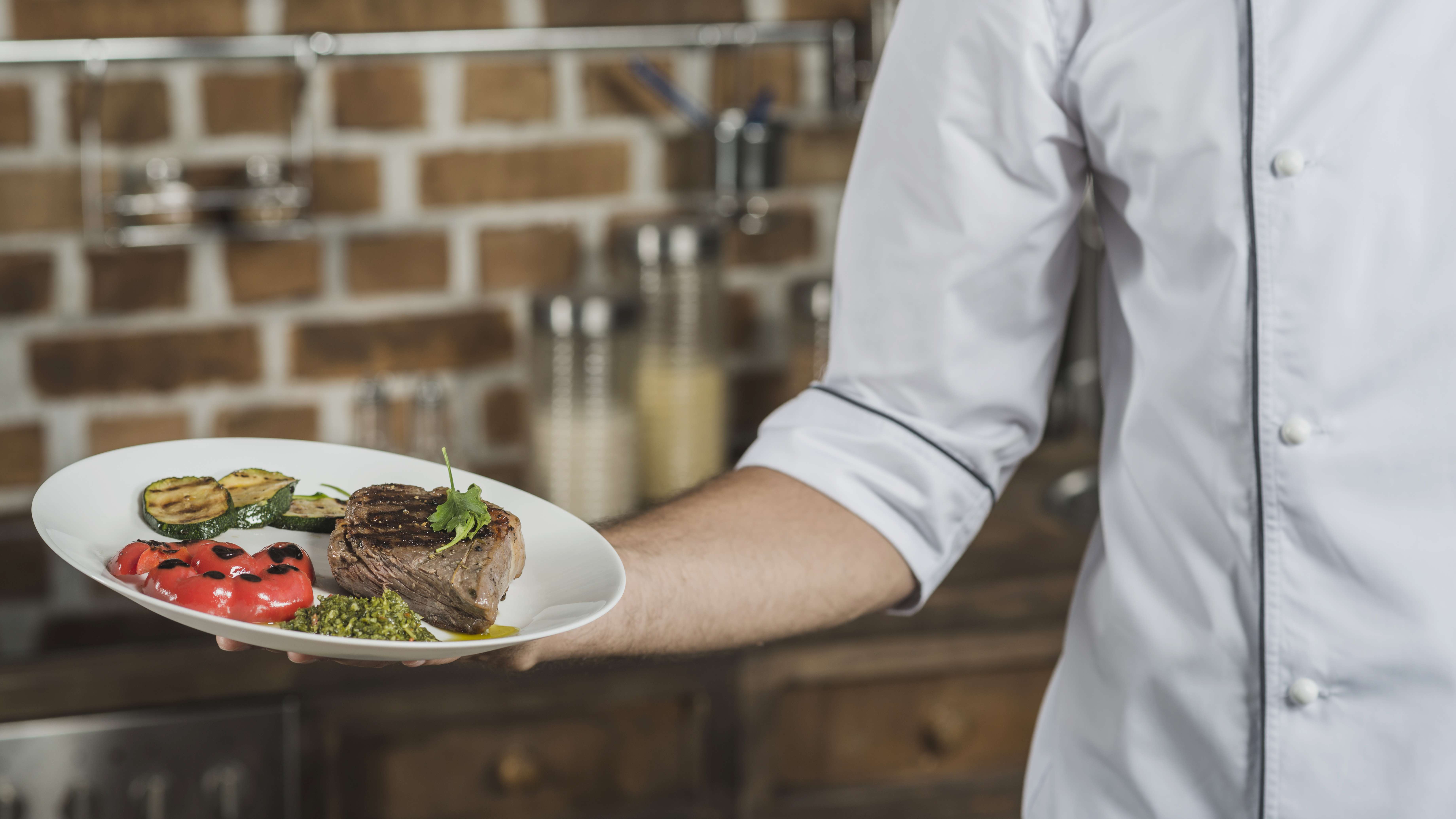 Chef de cozinha de dólmã branca segurando um prato com carne e vegetais, ilustrando o impacto do imposto seletivo no food service.