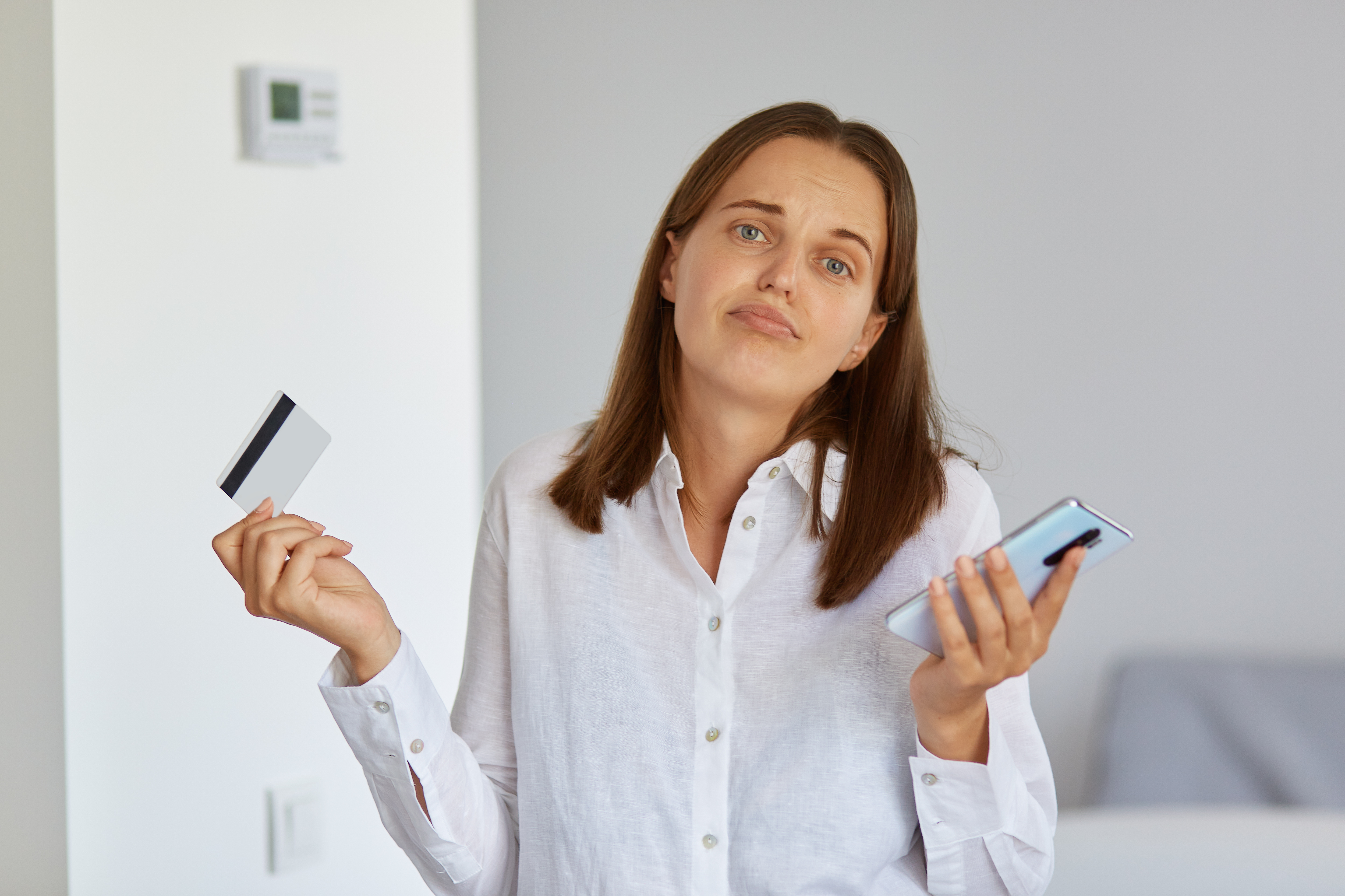 Mulher de cabelo castanho com expressão de dúvida segurando um cartão de crédito e um smartphone, ilustrando os desafios e o impacto do split payment nos sistemas da empresa.
